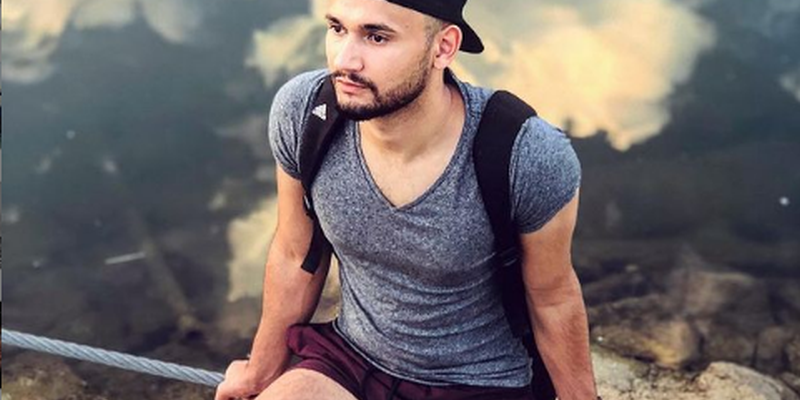 Ein junger Mann sitzt auf einem Relingdrahtseil am Neckar, im Hintergrund ist der Neckarstrand in Mannheim zu sehen.