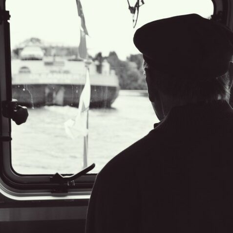 Blick über die Schulter eines Mannes mit Mütze. Der Mann blickt durch eine Scheibe auf ein anderes Schiff.